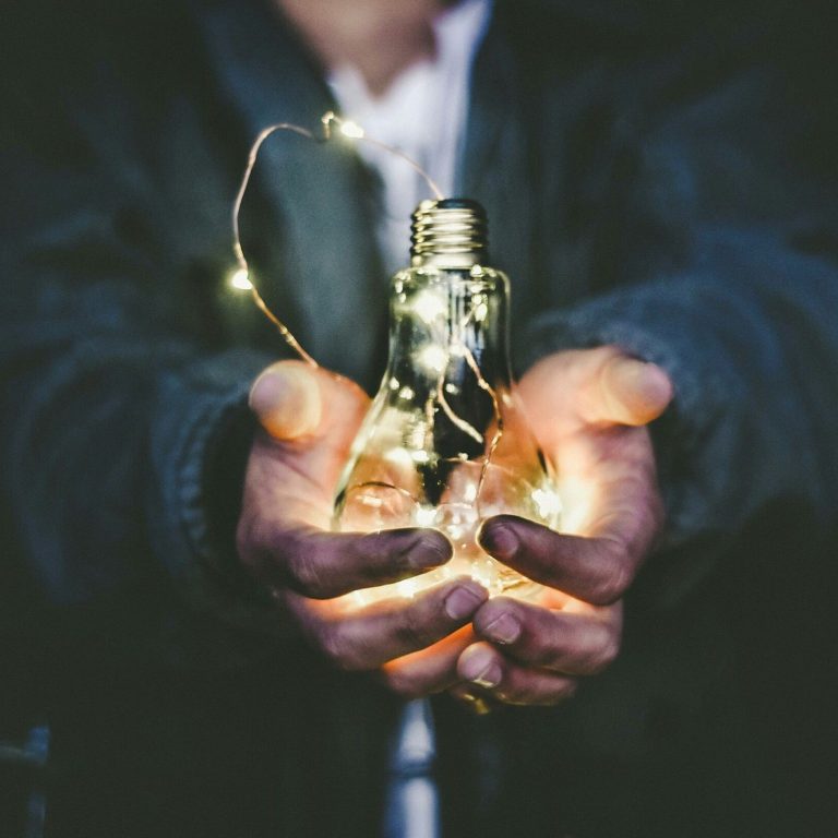Sierlijke handen houden een gloeilamp, symbool voor helende energie en licht